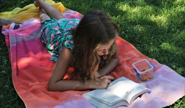 girl in pink dress reading book on green grass during daytime